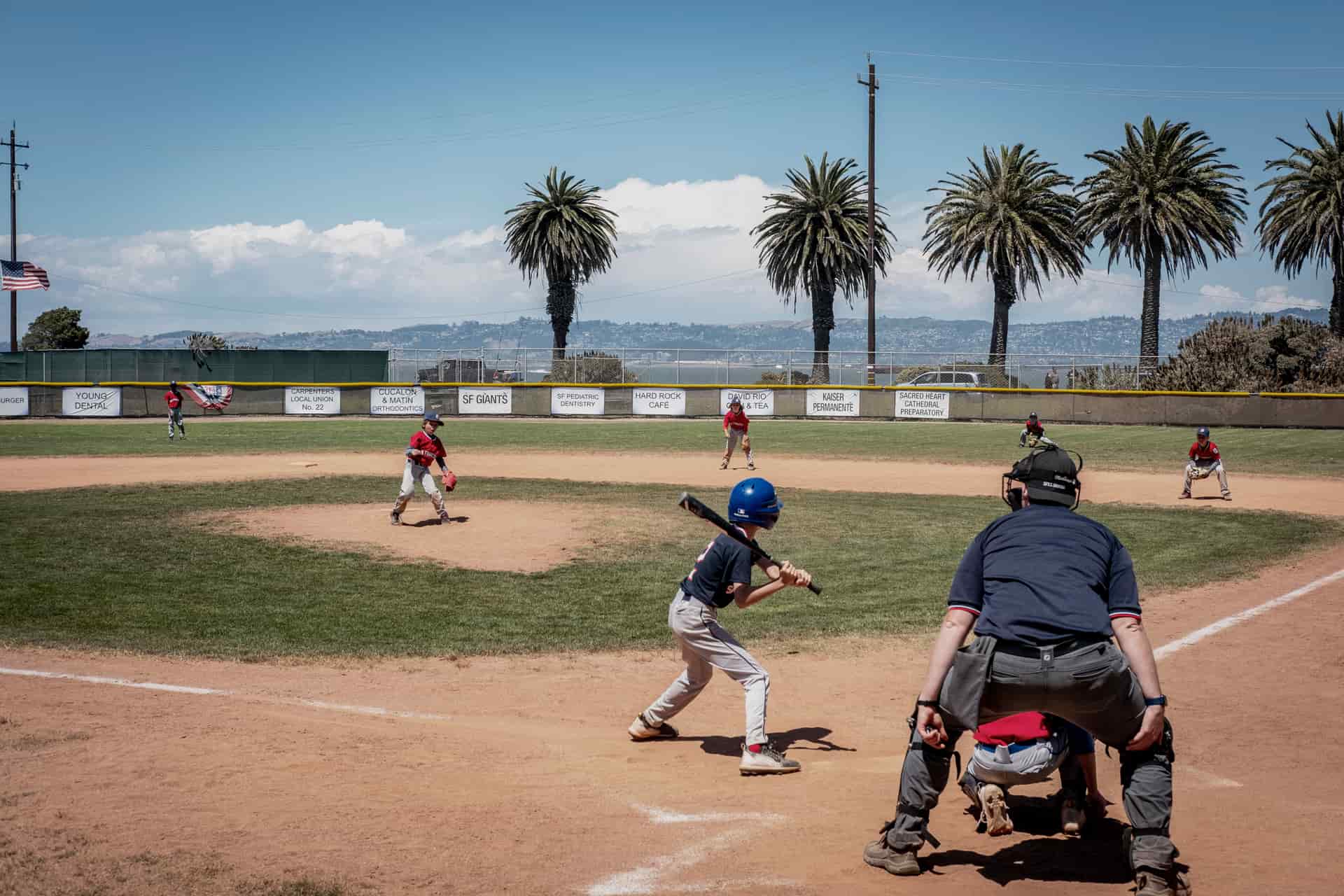 Kids playing baseball on a sunny field with palm trees and mountains behind