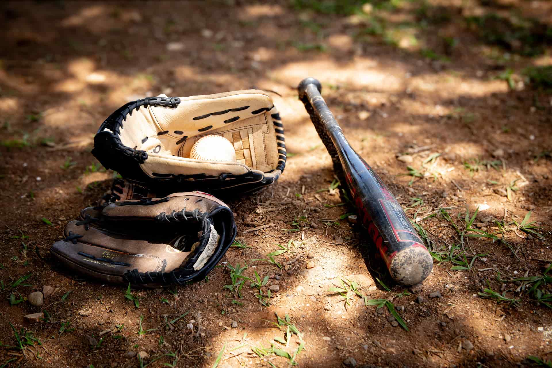 Illustrative stock photo: a glove, bat and ball on a dusty outdoor field