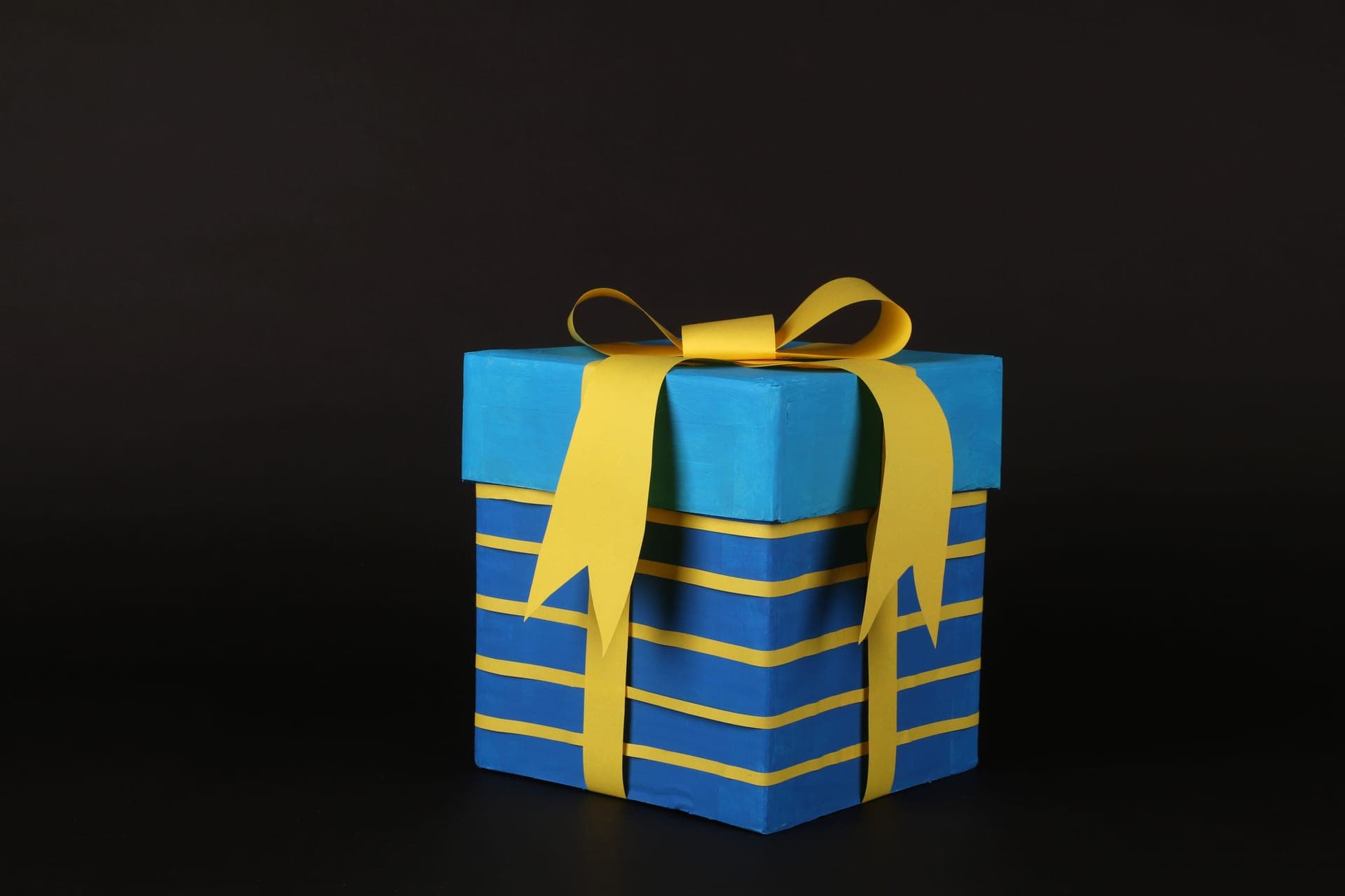 A blue gift box tied with a yellow ribbon on a dark background